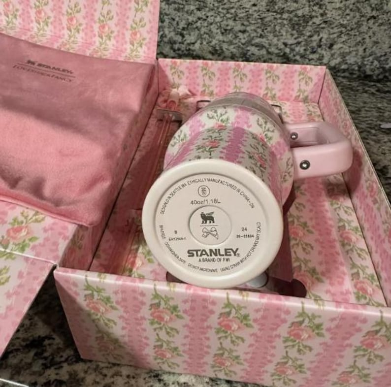 May include: A pink and floral Stanley mug with a matching pink handle and lid, presented in a decorative box. The box and mug feature a pink floral pattern. The mug is 40oz/1.18L.