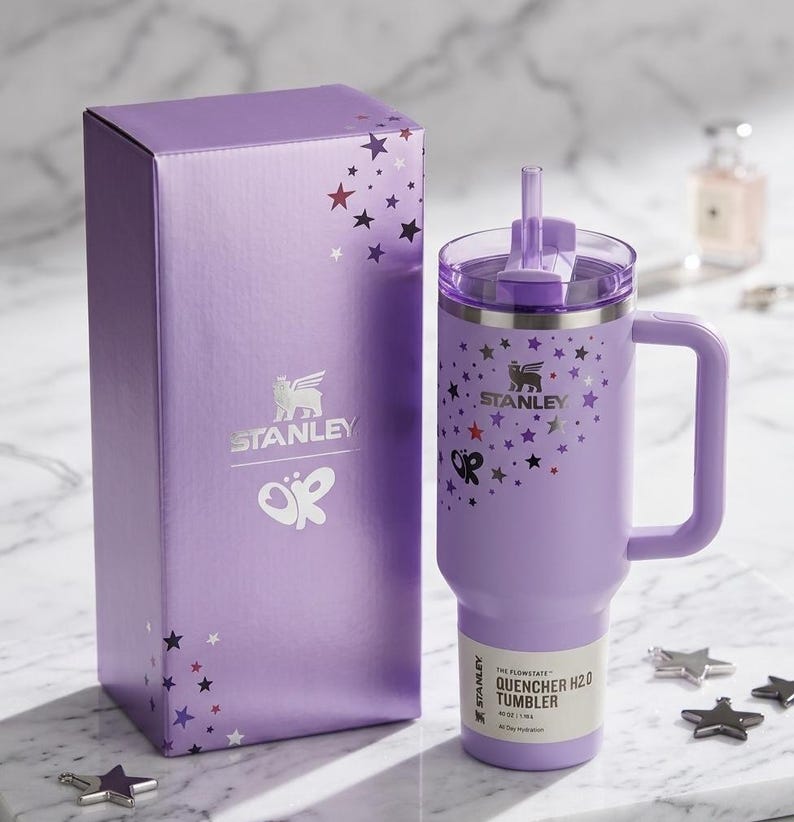 Puede incluir: Un vaso Stanley Quencher H2.0 lavanda con asa y caja de regalo a juego. Tanto el vaso como la caja presentan un dise&ntilde;o de estrellas y el logotipo de Stanley. El vaso tiene una pajita y una etiqueta que dice "All-Day Hydration".