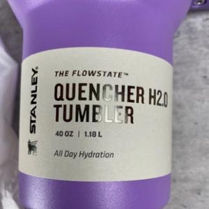 Puede incluir: Un vaso Stanley Quencher H2.0 morado. El vaso tiene una capacidad de 1,18 L y presenta el texto "All Day Hydration". El producto es de la colecci&oacute;n "The Flowstate".