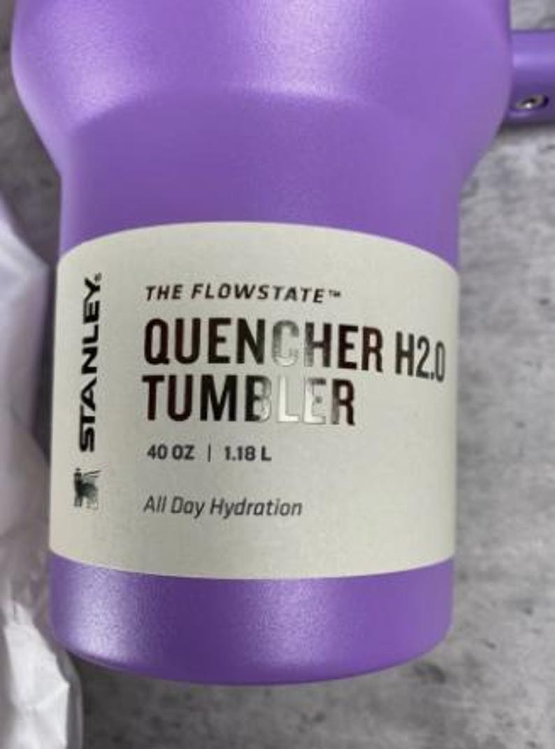 Puede incluir: Un vaso Stanley Quencher H2.0 morado. El vaso tiene una capacidad de 1,18 L y presenta el texto "All Day Hydration". El producto es de la colecci&oacute;n "The Flowstate".