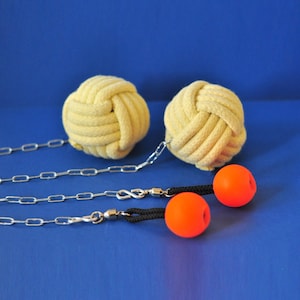 May include: Two yellow rope balls with silver chains and orange balls attached. The rope balls are knotted and have a textured appearance. The orange balls are smooth and round. The background is a solid blue.