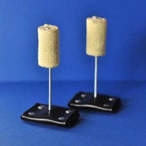 以下が含まれることがあります： 円筒形の2つの火のポイヘッド。ベージュ色の織り素材で作られています。銀色のロッドに取り付けられ、銀色のリベットが付いた黒い革のベースに取り付けられています。背景は無地の青色です。