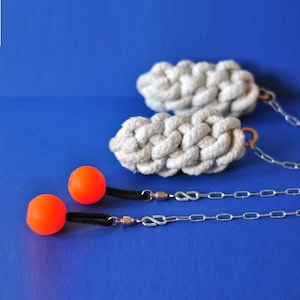 Peut inclure: Deux balles de jonglage oranges avec des cordons noirs et des chaînes argentées sont présentées à côté de deux balles en corde tressée blanches. Les objets sont posés sur un fond bleu uni. Les balles de jonglage sont rondes et orange vif.