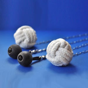 May include: Two white rope balls with black, round handles connected by silver chains. The rope balls are knotted, and the handles are attached to the chains with black cords. The background is a solid blue.