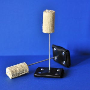 May include: Three fire poi props on a blue background. Each poi consists of a cylindrical, beige fire wick attached to a metal rod and a black leather base. The wicks are made of a woven material.