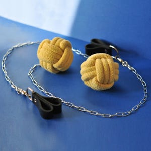 May include: A set of two yellow rope knot balls connected by a silver chain, with black leather handles. The items are set against a blue background.