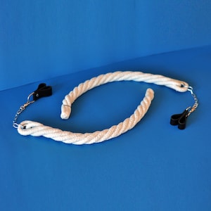 Op de afbeelding: Twee witte touwbeugels met zwarte, leerachtige clips en zilverkleurige kettingbevestigingen. De touwen zijn in een gebogen vorm gerangschikt tegen een blauwe achtergrond. De clips zijn aan de uiteinden van de touwen bevestigd.