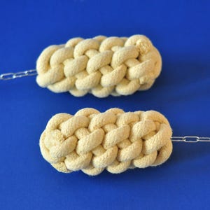 May include: Two cream-colored, woven rope door pulls with silver-colored chain attachments. The door pulls are oval-shaped and have a textured, braided appearance. The background is a solid, bright blue.