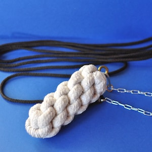 Può includere: Un guinzaglio per cani in corda intrecciata color crema, con una catena color argento e una corda nera. Il guinzaglio è appoggiato su una superficie blu. La sezione intrecciata è lunga circa 15 cm.