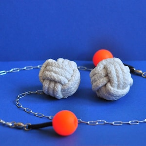 Op de afbeelding: Een set van drie grijze touwknopen met oranje bollen en een zilveren ketting op een blauwe achtergrond. De knopen zijn strak gewikkeld en de bollen zijn gelijkmatig verdeeld. De ketting verbindt de knopen en bollen.