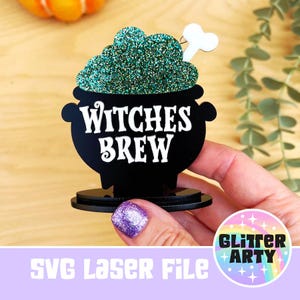 May include: A black cauldron-shaped decoration with the words "Witches Brew" in white. The cauldron is filled with green glitter and a small white bone. The image also includes the text "SVG Laser File".
