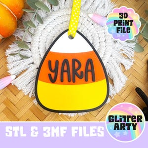 May include: A candy corn shaped ornament featuring a white top, orange middle, and yellow bottom with the name YARA in black raised letters. A yellow ribbon with white polka dots is attached to the top. The text 3D PRINT FILE and STL & 3MF FILES are visible.