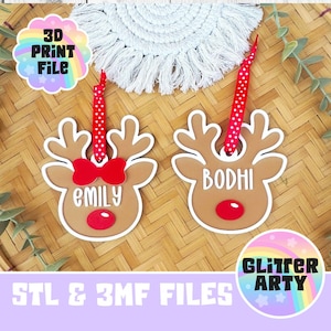 May include: Two tan reindeer-shaped ornaments with white outlines, red noses, and red polka-dot ribbon hangers. One ornament features a red bow and the name Emily, while the other features the name Bodhi. Text reads 3D PRINT FILE and GLITTER ARTY.