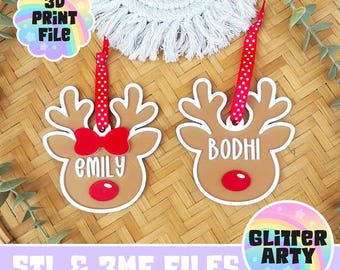 May include: Two tan reindeer-shaped ornaments with white outlines, red noses, and red polka-dot ribbon hangers. One ornament features a red bow and the name Emily, while the other features the name Bodhi. Text reads 3D PRINT FILE and GLITTER ARTY.