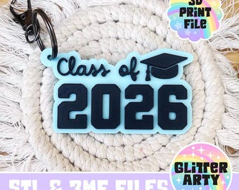 May include: A light blue keychain with the text "Class of 2026" and a graduation cap. The keychain has a black metal clasp and ring. The background is a cream-colored macrame coaster. The image also includes the text "3D PRINT FILE" and "Glitter Arty".