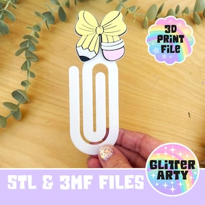 May include: A white paperclip-shaped bookmark with a yellow bow and pencil design. The bookmark has the text "3D PRINT FILE" and "STL & 3MF FILES". The image also includes a "Glitter Arty" logo.