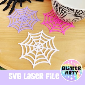 May include: Three spiderweb-shaped coasters in purple, pink, and white. A decorative bowl sits atop a pink coaster. The image includes the text "SVG Laser File" and a logo that says "Glitter Arty".