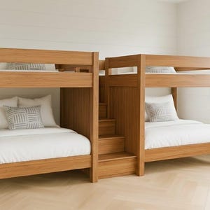 Puede incluir: Dos literas de madera con acabado marrón claro. Cada cama tiene una litera superior e inferior con ropa de cama blanca y almohadas estampadas. Una pequeña escalera da acceso a la litera superior. Las camas están en una habitación con paredes blancas y suelo de madera clara.