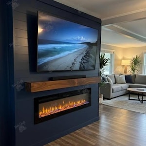 May include: A dark navy blue shiplap wall feature with a mounted flat-screen television displaying a beach scene, a natural wood mantel shelf, and a rectangular electric fireplace insert with glowing orange flames set into the wall structure.