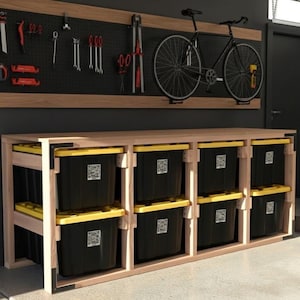May include: A garage storage unit with a wooden frame and black bins with yellow lids. A black pegboard with tools and a mounted bicycle are on the wall above the unit. The tools include wrenches, pliers, and screwdrivers.