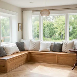 Puede incluir: Un acogedor asiento junto a la ventana con un banco de madera, adornado con varias almohadas en blanco, gris y beige. La habitación cuenta con grandes ventanas con cortinas blancas, una pequeña mesa redonda y una lámpara colgante tejida.