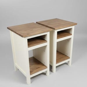 May include: Two matching wooden nightstands. Each nightstand has a light cream-colored frame with a natural wood top and two open shelves. The nightstands are designed with a simple, rustic aesthetic.