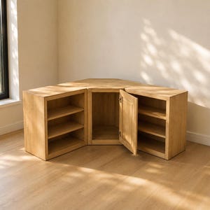 Könnte beinhalten: Ein Eckschrank aus hellem Eichenholz mit modularem Design und drei separaten Abschnitten. Die linken und rechten Einheiten verfügen über offene Regale, während das mittlere Element eine Flügeltür besitzt, die einen Stauraum freigibt.