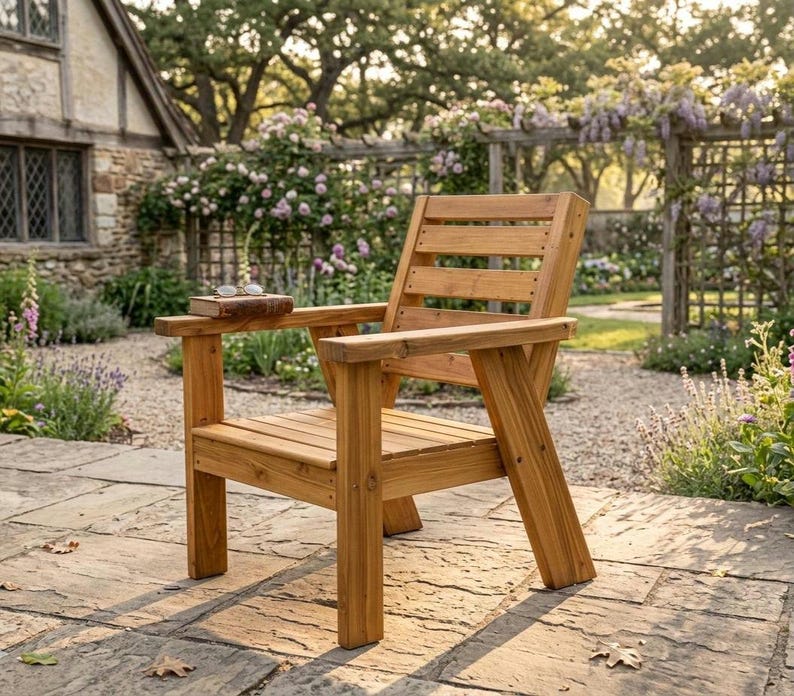 以下が含まれることがあります： 背もたれとアームレストが付いた木製の屋外用アームチェア。椅子は明るい色の木材でできており、石畳のパティオに置かれています。本と眼鏡がアームレストに置かれています。背景には庭と石造りの建物があります。