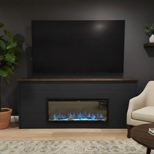 May include: A contemporary living room scene with a large black television above a dark blue fireplace with a simulated flame effect. A potted plant and a beige armchair are also visible.