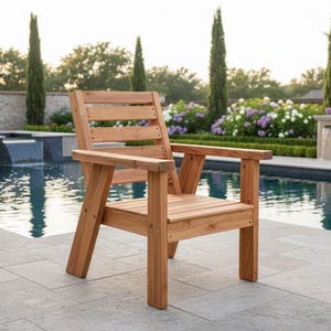 以下が含まれることがあります： 天然仕上げの木製アウトドアチェア。背もたれとアームレストはスラット仕様です。プールサイドの石畳のパティオに配置されています。椅子は木製で、屋外での使用を目的として設計されています。