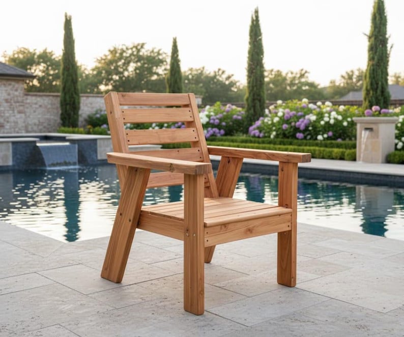 以下が含まれることがあります： 天然仕上げの木製アウトドアチェア。背もたれとアームレストはスラット仕様です。プールサイドの石畳のパティオに配置されています。椅子は木製で、屋外での使用を目的として設計されています。