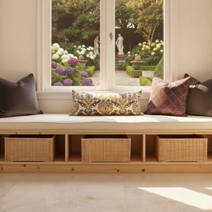 May include: A window seat with a cream-colored cushion and three decorative pillows in shades of brown and burgundy. Below the seat are three woven wicker baskets. The window overlooks a garden with flowers and statues.