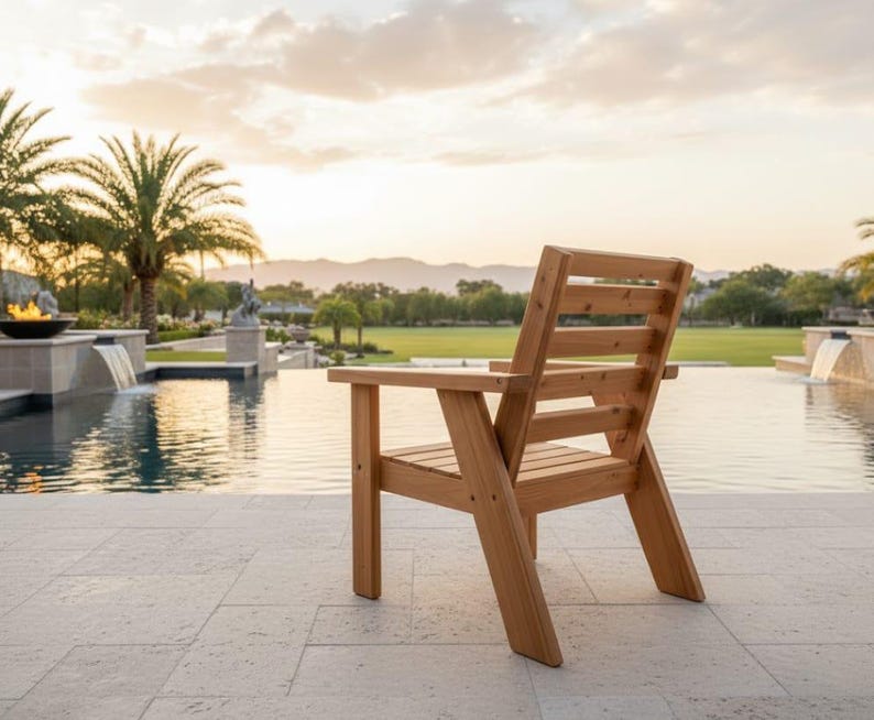 以下が含まれることがあります： スラットバックとアームレストを備えた木製のアウトドアチェア。椅子は明るい色の木材で作られており、石のパティオに配置されています。背景にはプール、ヤシの木、美しい景色があります。
