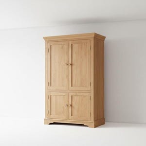 May include: A tall, light oak cabinet with four doors and brass-colored knobs. The cabinet has a crown molding top and a base molding. The doors are flush with the frame. The cabinet is a light brown color and stands against a white wall.