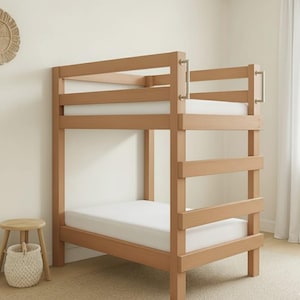 May include: A light-colored wooden bunk bed with a simple design. The bed has two levels, each with a white mattress. The frame is made of light-colored wood, and there are metal handles on the side for climbing. The bed is in a room with neutral-colored walls.