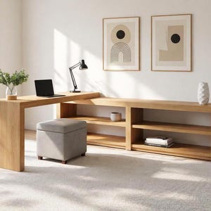 May include: A modern home office setup featuring a light wood desk with an attached shelving unit. A laptop, black desk lamp, and a gray ottoman are present. Two framed abstract art pieces hang on the wall, and a potted plant adds a touch of greenery.