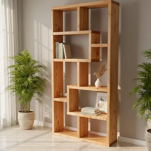 Puede incluir: Una estantería alta de madera clara con un diseño asimétrico. Los estantes contienen libros, un pequeño jarrón blanco con flores secas y una imagen enmarcada. Dos plantas en macetas flanquean la estantería, añadiendo un toque de vegetación.