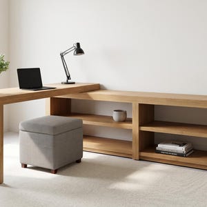 May include: A light wood desk with a built-in bookshelf and a gray ottoman. A black laptop and a black desk lamp are on the desk. A white vase and a small ceramic pot are on the bookshelf. The desk is 100 inches long.