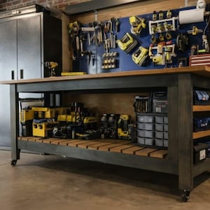 May include: A robust workbench with a dark grey frame and a natural wood top. The workbench has a lower shelf and side shelves for storage. Tools are organised on a blue pegboard above the workbench, and various power tools are stored below.