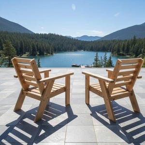 以下が含まれることがあります： アームレスト付きの木製椅子が2脚、石畳のパティオに置かれ、湖と山脈を望んでいます。椅子は明るい色の木材で作られており、日光の下で影を落としています。