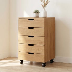 May include: A light oak wood storage unit featuring five horizontal drawers with integrated cutout handles. The rectangular cabinet is supported by four black swivel castors, allowing for mobility. The top surface holds a small potted succulent.