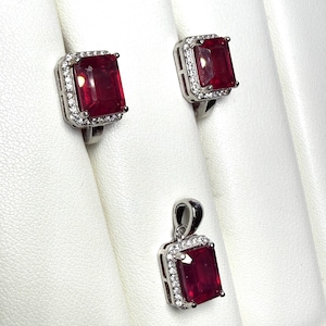 May include: A jewelry set featuring a ring and pendant with a large, rectangular, deep red gemstone. The gemstones are surrounded by a halo of smaller, clear stones, set in a silver-colored metal.