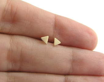 Könnte beinhalten: Ein Paar goldene Dreiecks-Ohrstecker. Die Ohrringe sind klein und zart und perfekt für den Alltag.