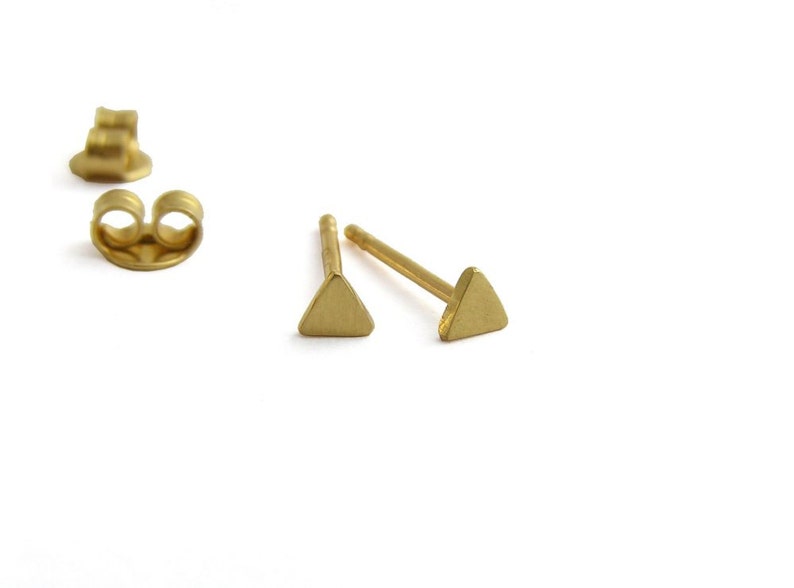 May include: A pair of gold triangle stud earrings. The earrings are small and simple, with a minimalist design.