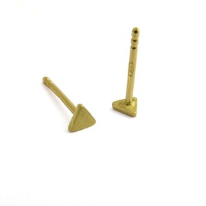 May include: A pair of gold triangle stud earrings. The earrings are small and simple, with a minimalist design.