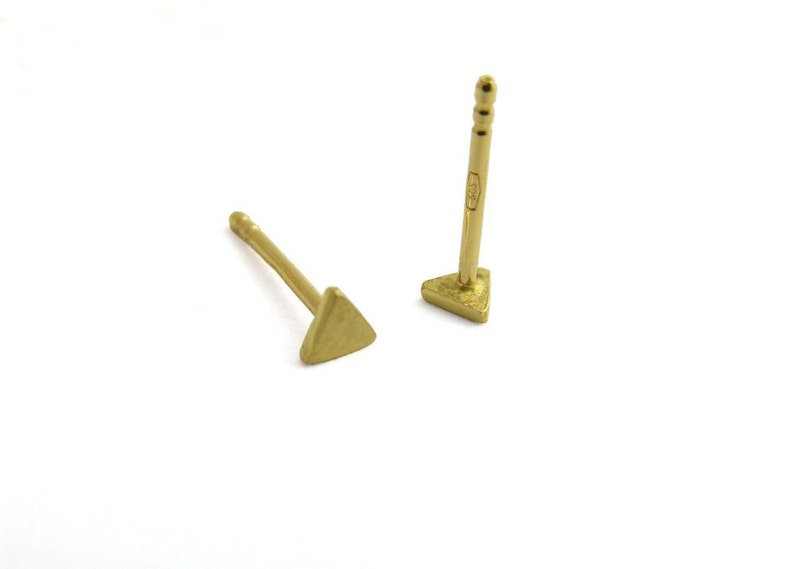 May include: A pair of gold triangle stud earrings. The earrings are small and simple, with a minimalist design.