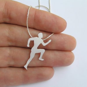 May include: Silver necklace with a runner pendant. The pendant is a silhouette of a person running.