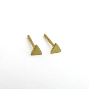 May include: A pair of gold triangle stud earrings. The earrings are small and simple, making them a versatile accessory for any occasion.