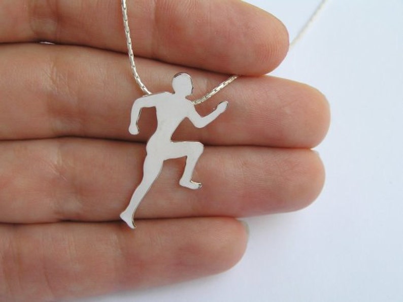 May include: A silver necklace with a pendant shaped like a running person. The pendant is a silhouette of a person running with their arms outstretched.