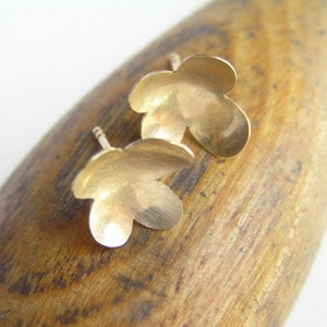 May include: A pair of gold flower-shaped stud earrings. The earrings are small and delicate, with a smooth, polished finish.